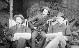Three men sitting in deckchairs, smoking pipes and reading papers.