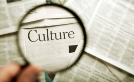 A hand holding a magnifying glass over a newspaper that has the word "culture" by fotosipsak via Canva