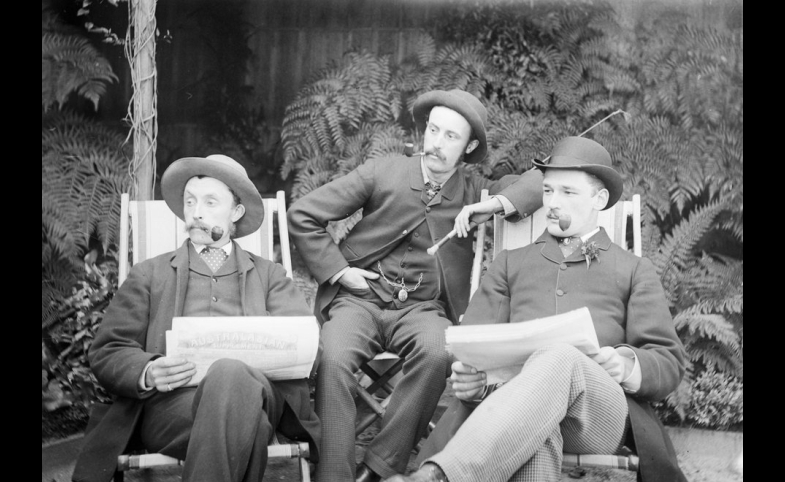 Three men sitting in deckchairs, smoking pipes and reading papers.