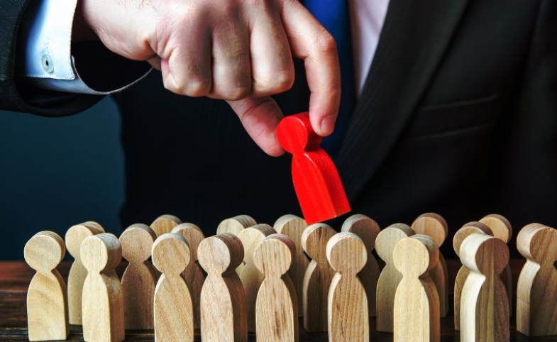 A man pulls the red wooden peg doll out of the crowd by Dorin Tamas via Canva